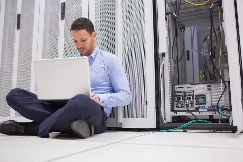Man sitting on floor with laptop beside servers in data center