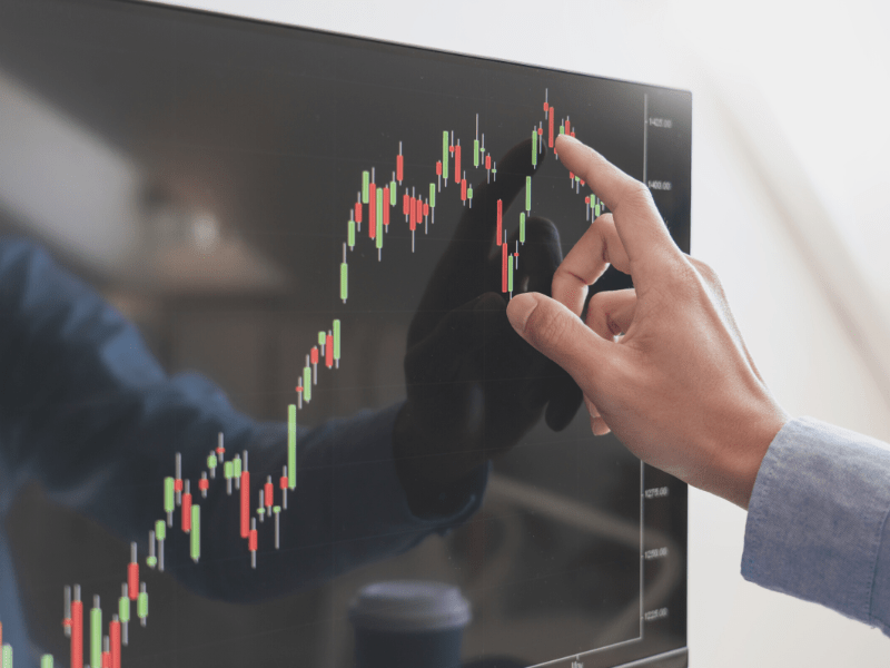 A man pointing at a stock chart on a screen, analyzing market trends. Relevant to digital marketing industry and business brokers.