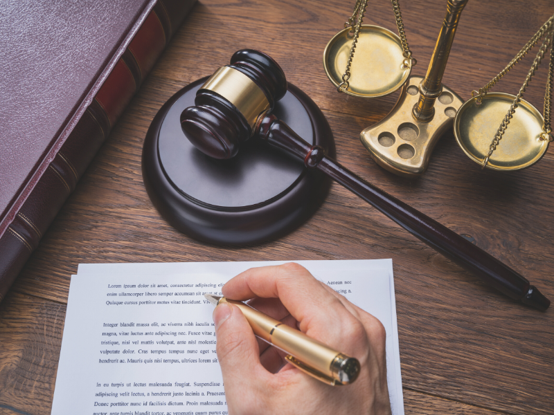 A lawyer's hand writes on paper with a gavel and scales of justice, symbolizing the legal industry we serve in the digital marketing field.